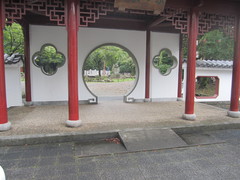 朱色の柱と白壁の杭州門の写真。道路から杭州門を通るには段差が１段あり、中央にスロープもあります。