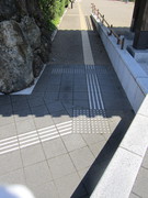 正門前のスロープの写真。正門前には５段ほどの階段がありますが、横にスロープがあり点字ブロックも敷かれています。