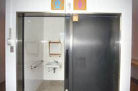 屋外のトイレの写真。駐車場側の高い石垣の一角に車いすマークのトイレがあります