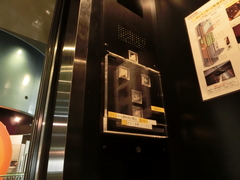 車いすで1階から地下に降りる際に使うエレベーターのカバー付きボタンの写真。「タイムスリップエレベーター」として展示の一部として使用されています