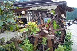 水車の似合う風景の写真。合掌造り集落の風情に、緑の庭木に囲まれた水車が溶け込んでいます。