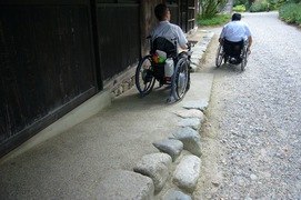 受付の建物から園内に通じるスロープの写真。スロープを降りたところから砂利道になっていて、車いすの場合は前輪が砂利に埋まってしまうため、単独での通行は困難です。