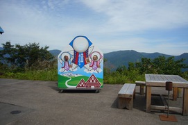 顔を出して、「はい、チーズ」。の写真。白山連峰をバックに、飛騨に伝わる「さるぼぼ」の顔出しパネルで記念撮影。